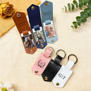 May include: Leather keychains in brown, navy, and blue with personalized photos and text. The keychains have a snap closure and a metal keyring. Additional keychains in pink, black, and white with initials and a decorative emblem.