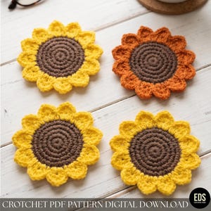 May include: Four handmade crochet sunflower coasters. The coasters feature a yellow petal design with a brown center. One coaster is orange. The coasters are arranged on a white wooden surface. The text "CROCHET PDF PATTERN DIGITAL DOWNLOAD" is at the bottom.