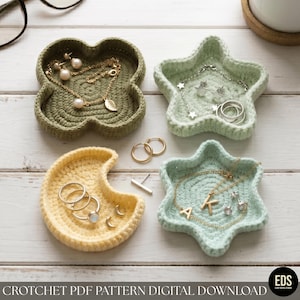 May include: Four crocheted trinket dishes in olive green, pale mint, and soft yellow. The dishes are shaped like a four-leaf clover, two stars, and a crescent moon. They contain various gold and silver jewelry pieces including necklaces, rings, and earrings.