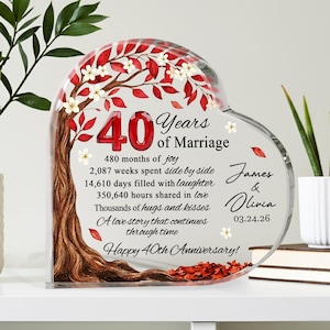 May include: A heart-shaped acrylic anniversary gift with a tree design. The number "40" is in red, with text that reads "Years of Marriage" and a list of milestones. The names "James & Olivia" and the date "03.24.26" are also included.