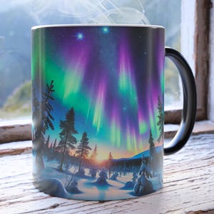 May include: A black handled mug featuring a vibrant depiction of the Aurora Borealis. The design showcases a colorful display of green and purple lights over a snowy landscape with trees. Steam rises from the mug, suggesting a hot beverage.