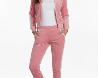 May include: A pink velour tracksuit with white stripes on the sleeves and sides of the trousers. The jacket has a zip closure and the trousers have pockets. The outfit is paired with pink trainers.