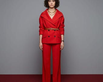 May include: A striking red suit comprising a double-breasted jacket with a brown belt and wide-leg trousers. The jacket has black buttons and a notched collar. A gold chain necklace and a black watch complete the outfit. The ensemble is worn with brown pointed-toe shoes.