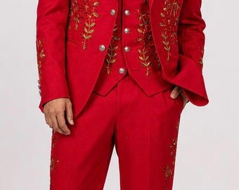 May include: A bright red suit consisting of a blazer, a waistcoat, and trousers. The blazer and waistcoat feature intricate gold and red floral embroidery along the lapels and front panels. The trousers also display matching floral embroidery down the sides.