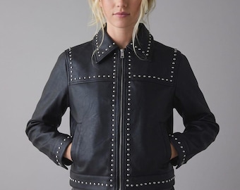 May include: Black leather jacket with silver stud detailing. The jacket has a collared neckline, a front zip, and pockets. Silver studs are arranged on the collar, shoulders, front, and cuffs. The jacket is worn with a dark belt and blue jeans.