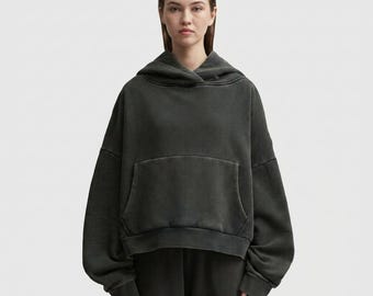 May include: A dark grey hoodie with a kangaroo pocket and a drawstring hood. The hoodie is part of a matching set and has a slightly faded, vintage look. The model is wearing the hoodie and matching trousers.