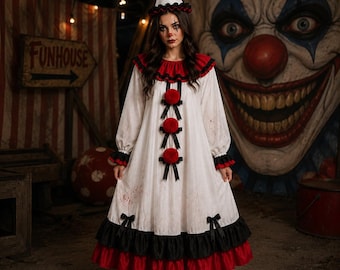 May include: A white clown dress featuring a red ruffled collar, three red pom-poms with black ribbons down the front, and a black and red ruffled hem. The dress has long sleeves with ruffled cuffs and is paired with a matching white cone hat.