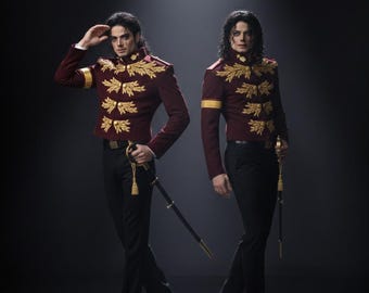 May include: Two figures in burgundy jackets with gold embroidery and black trousers stand in a spotlight. The jackets have gold accents on the sleeves and shoulders. Each figure holds a sword. The background is dark.