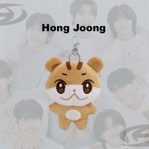 May include: A plush keychain featuring a cartoon tiger with brown and white fur, large brown eyes, and a smiling face. The keychain has a silver clasp. The text "Hong Joong" is above the plush toy.