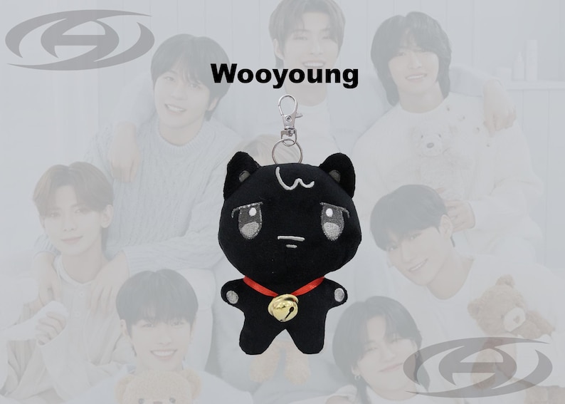 May include: Black plush cat keychain with a red collar and gold bell. The cat has white accents and large eyes. The word "Wooyoung" is above the cat. The background features a group of people.