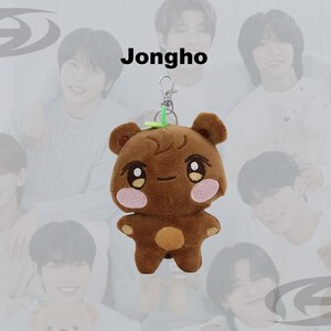 May include: Brown plush bear keychain with a green leaf accent. The bear has a cute face with pink cheeks and a small orange belly. The word "Jongho" is written above the bear.
