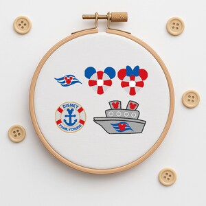 Pode incluir: Um bastidor de bordado com desenhos temáticos da Disney. Os desenhos incluem um navio de cruzeiro, boias salva-vidas em forma de Mickey Mouse e um logotipo que diz "Disney Family Cruise". Botões de madeira circundam o bastidor.