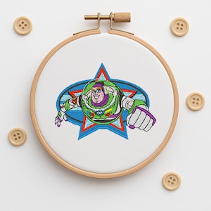 May include: Embroidered hoop art featuring Buzz Lightyear from Toy Story. The design shows Buzz in his spacesuit, set against a blue star and oval background. The embroidery is in vibrant green, purple, white, and red. Wooden buttons surround the hoop.