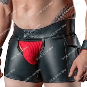 Op de afbeelding: Zwarte leren shorts met een rode zakinzet. De shorts hebben een brede tailleband met knoopdetails en kleine zakken. Bijpassende zwarte polsbanden met rode rand zijn ook zichtbaar.