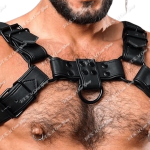 May include: Black leather chest harness with adjustable straps and metal buckles. The harness features a central ring and is designed to be worn across the chest and shoulders. The product is designed for the adult novelty market.
