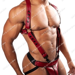 May include: Red leather harness with black hardware. The harness features adjustable straps and a jockstrap design. The product is designed for a body-positive fit. The image shows the product on a person.