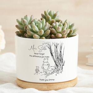 Puede incluir: Maceta de cerámica blanca con una planta suculenta. La maceta presenta una ilustración de Winnie the Pooh y el texto "Sra. Smith, Nunca olvides la diferencia que haces. Gracias, Emma."