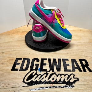 Pu&ograve; includere: Sneakers Nike Air Force 1 personalizzate in verde acqua, rosa, viola, giallo e blu. Le sneakers hanno suole bianche e lacci rosa. La parola "Dragonair" &egrave; scritta sul lato. Il logo Nike &egrave; visibile sul tallone.