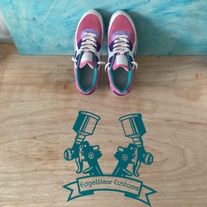 May include: Pair of pink, purple, and white athletic shoes with white laces. The shoes have a teal interior and are on a wooden surface. The image also features a teal graphic of two spray guns and the text "EdgeWear Customs".