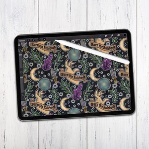 K&ouml;nnte beinhalten: Ein digitales Tablet-Bild mit einem sich wiederholenden Muster und dem Text "Burn the Rulebook". Das Design zeigt H&auml;nde, Kristalle, Monde, Dolche und florale Elemente in Lila, Gr&uuml;n und Gold auf schwarzem Hintergrund. Ein wei&szlig;er Stift liegt auf dem Bildschirm.
