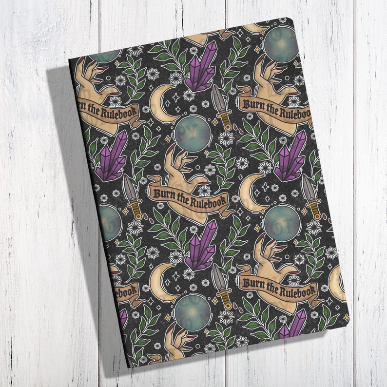 K&ouml;nnte beinhalten: Ein Notizbuch mit schwarzem Einband mit einem sich wiederholenden Muster aus H&auml;nden, Kristallen, Dolchen, Monden und dem Text "Burn the Rulebook". Das Design umfasst gr&uuml;ne Bl&auml;tter und kleine wei&szlig;e Blumen. Das Gesamtthema ist mystisch.