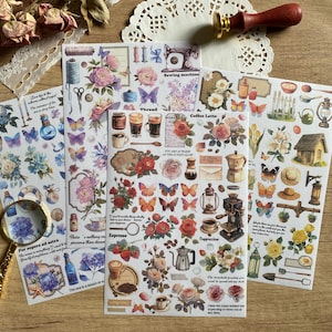 May include: A collection of decorative stickers with floral, butterfly, and coffee-themed designs. The stickers feature text like "Sewing machine", "Coffee Latte", and "Espresso". A magnifying glass, dried flowers, and lace embellishments are also present.