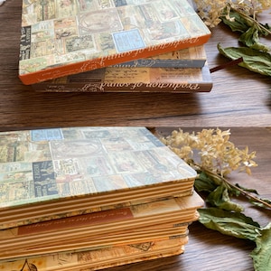 May include: A stack of three vintage-style notebooks. The covers are adorned with a collage of antique images and text. The edges of the notebooks are a warm orange and brown. The words "Production of sound" are printed on the spine.