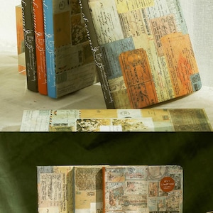 May include: A collection of vintage-style journals with covers adorned with a collage of aged paper, stamps, and handwritten script. The spines are in various colors, including brown, orange, and blue. The journals are stacked and displayed.