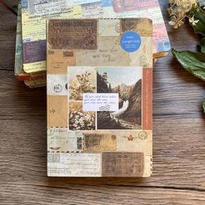 May include: A stack of vintage-style journals with covers adorned with postage stamps, postcards, and handwritten letters. The top journal features a landscape scene and the text "If you shed tears when you miss the sea, you also miss the stars."