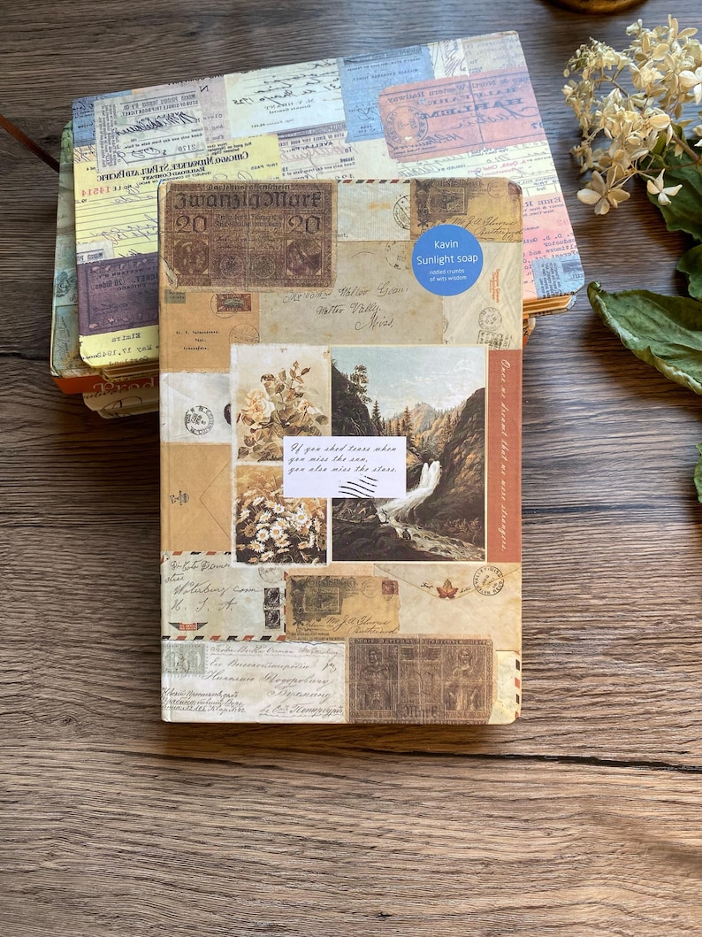 May include: A stack of vintage-style journals with covers adorned with postage stamps, postcards, and handwritten letters. The top journal features a landscape scene and the text "If you shed tears when you miss the sea, you also miss the stars."