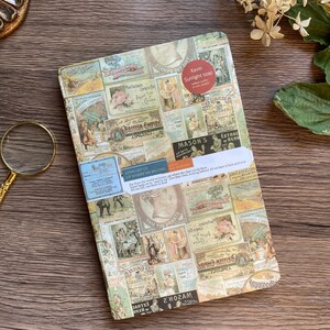 May include: A rectangular notebook with a collage of vintage-style labels and stamps. The notebook has a sticker that reads "Kavin Sunlight soap." The background is a wooden surface. The notebook is a unique stationery item.