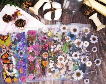 Puede incluir: Pegatinas florales con mariposas y diversas flores en tonos rosa, morado, amarillo y blanco. Las pegatinas están en un embalaje de plástico transparente, con elementos decorativos como piñas y algodón.