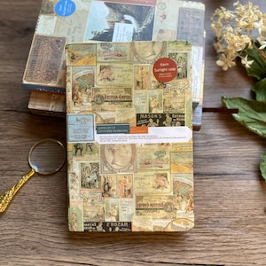 May include: A stack of vintage-style boxes with a collage of old advertisements and labels. The top box has a blue sticker. The front box features the text "Kavin Sunlight soap" and "British Empire". A magnifying glass rests nearby.