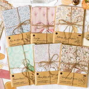 May include: Several stationery sets are displayed, each tied with twine and featuring patterned paper and decorative labels. The sets showcase floral and botanical designs, with text labels including "Sun to star set" and "Autumn flowers". The colour scheme includes soft pastels and earth tones.