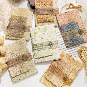 Op de afbeelding: Een verzameling handgemaakt papier met diverse texturen en kleuren, waaronder beige, bruin en roze. Elk stuk is versierd met decoratieve papieren stroken en tekst, zoals "Soft Memory" en "Color Page Collection". Ideaal voor scrapbooking en journaling.