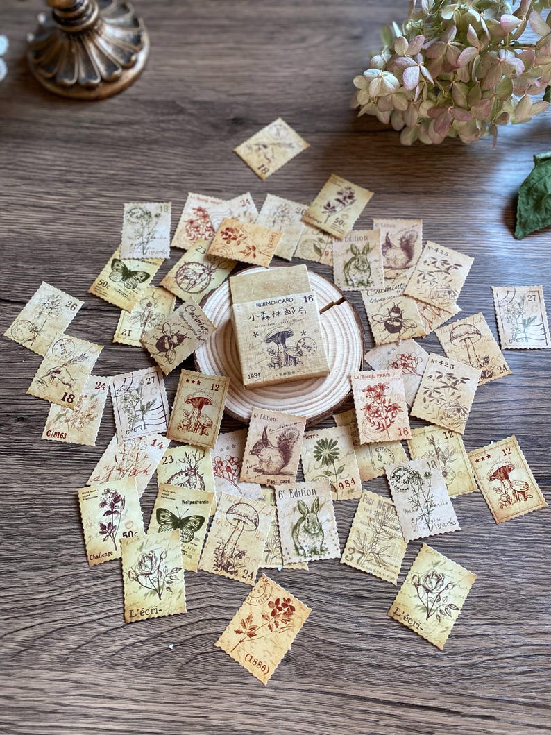 May include: A collection of vintage-style paper ephemera, including stamps and a small box, featuring botanical and animal illustrations. The stamps have torn edges and various numbers and text. The box has Japanese text and mushroom illustrations.