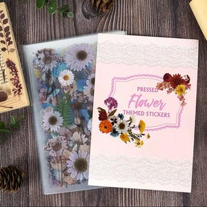 Puede incluir: Una funda de pl&aacute;stico transparente llena de flores prensadas y una tarjeta rosa con el texto "PRESSED Flower THEMED STICKERS". La tarjeta tiene un borde de encaje blanco y un dise&ntilde;o floral.