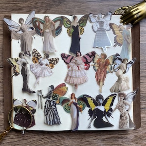 May include: A selection of vintage fairy stickers with butterfly wings, in various dresses and poses. The stickers are arranged on a notebook page, with a magnifying glass and decorative hand in the image.