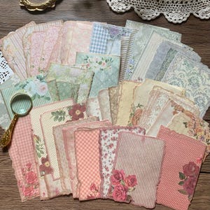 May include: A collection of vintage-style paper sheets in various pastel colors, including pink, green, and beige. The papers feature floral patterns, stripes, and polka dots, with torn edges for a distressed look. A gold-toned magnifying glass is visible.