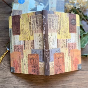 May include: Open notebook with a vintage ticket collage design. The cover and pages feature a mix of colorful, aged tickets and ephemera. The spine reads "Production of sound" in elegant script. A decorative item for writing and journaling.