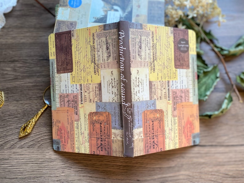 May include: Open notebook with a vintage ticket collage design. The cover and pages feature a mix of colorful, aged tickets and ephemera. The spine reads "Production of sound" in elegant script. A decorative item for writing and journaling.