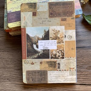 May include: A stack of vintage-style journals with covers adorned with postage stamps, old letters, and landscape imagery. The journals have a rustic, antique aesthetic, with a color palette of beige, brown, and cream. The top journal has a yellow cover.