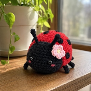 May include: A crocheted ladybug plush toy with a bright red body featuring black spots, a black head with two antennae, and shiny black eyes. A small, light pink crocheted flower with a yellow center is attached to the side of the head.