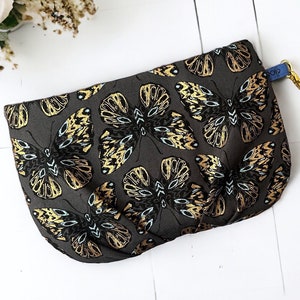 May include: A gray clutch purse with a gold butterfly print and a blue strap with the text "GLORY STAR SOCIETY".