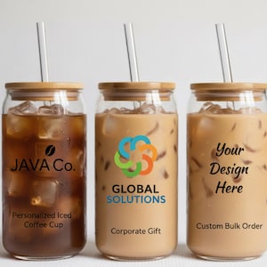 May include: Three glass iced coffee cups with bamboo lids and glass straws. The cups have different logos and text: "JAVA Co.", "GLOBAL SOLUTIONS", and "Your Design Here". The cups are filled with iced coffee.