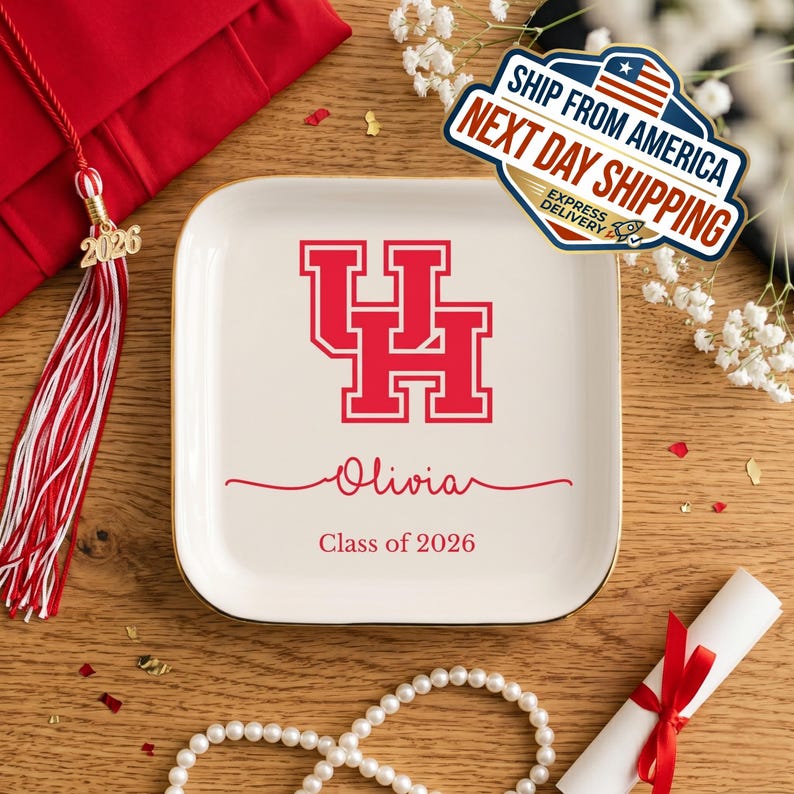 Puede incluir: Una bandeja cuadrada de cer&aacute;mica blanquecina con borde dorado, con un logotipo "UH" rojo, el nombre "Olivia" y "Class of 2026". Tem&aacute;tica de graduaci&oacute;n, con borla y diploma.