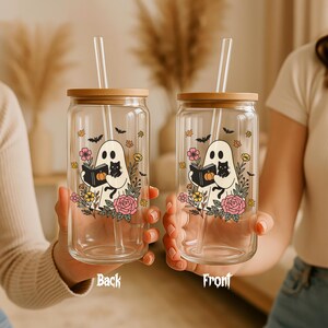 May include: Two clear glass tumblers with bamboo lids and glass straws. Each tumbler features a ghost illustration holding a book and a black cat, surrounded by flowers and bats. The text "Back" and "Front" are visible.