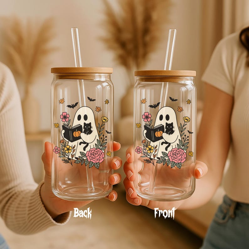 May include: Two clear glass tumblers with bamboo lids and glass straws. Each tumbler features a ghost illustration holding a book and a black cat, surrounded by flowers and bats. The text "Back" and "Front" are visible.