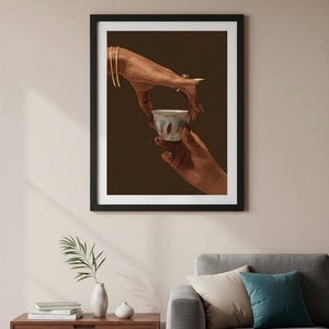 May include: Framed art print featuring two hands, one holding a small, ornate cup and the other reaching out. The artwork has a warm color palette with a dark brown background and a black frame. The hands are adorned with gold bracelets and rings.