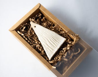 May include: A white, triangular ceramic ornament with a textured surface, displayed in a brown cardboard box with clear plastic sliding cover. The box is filled with brown crinkle paper for protection.